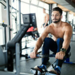 Young handsome man workout with rowing machine