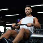 Fit and muscular man using rowing machine at gym.