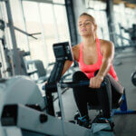 Young cute woman doing exercises with rowing machine